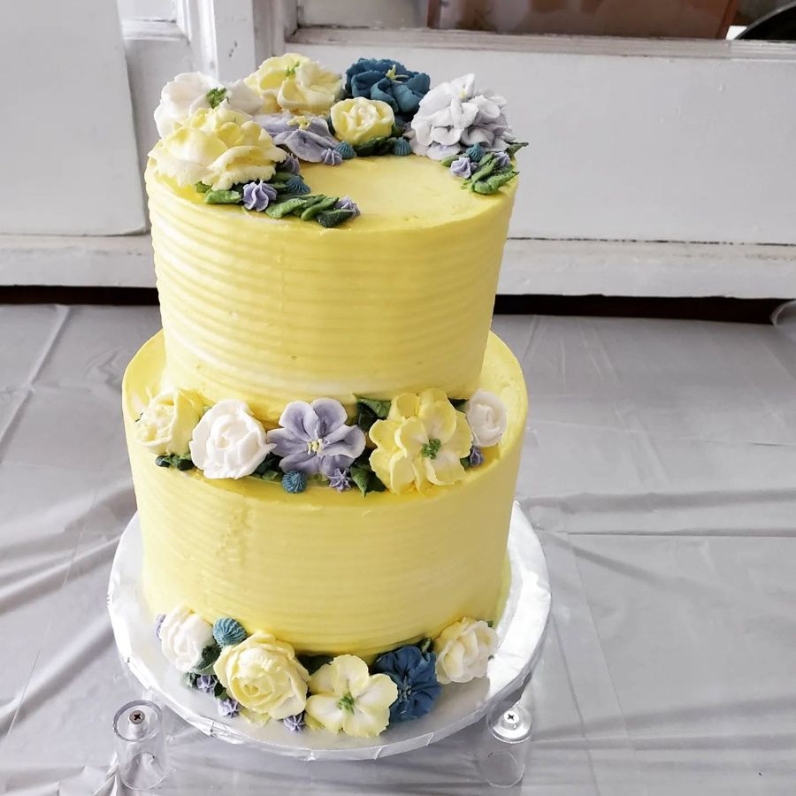 Two-tier yellow buttercream cake with piped white, blue and lavender flowers